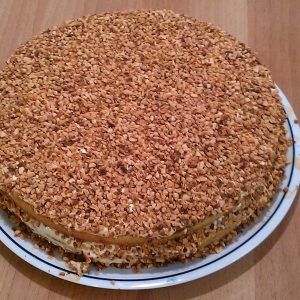 Torta rotonda alle nocciole tostate con strati di crema, dolce dessert su piatto bianco e blu, su tavolo di legno chiaro. Perfetta per feste.