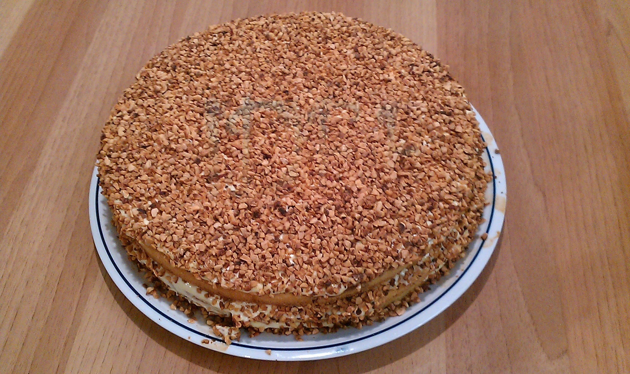 Torta rotonda alle nocciole tostate con strati di crema, dolce dessert su piatto bianco e blu, su tavolo di legno chiaro. Perfetta per feste.